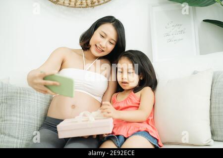 Felice attesa donna che fa selfie a suo marito. Casalinga incinta che parla sul telefono delle cellule con la sua famiglia. Foto Stock
