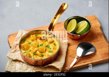 Korma di pollo in padella di rame su piano di cemento grigio. Piatto di curry di carne della cucina indiana con masala di latte di cocco. Cibo asiatico Foto Stock