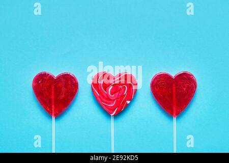 Concetto di giorno di San Valentino. Tre caramelle lollipop a forma di cuore su sfondo blu. Copia spazio per testo, vista dall'alto. Foto Stock