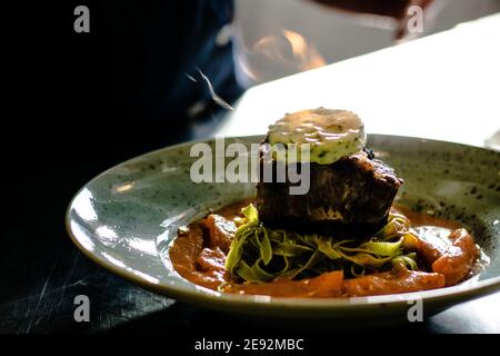 Bistecca di bue alla griglia e fiammato con tagliatelle di erbe verdi una purea di pomodoro in un ristorante Foto Stock