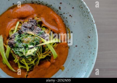 Bistecca di bue alla griglia e fiammato con tagliatelle di erbe verdi una purea di pomodoro in un ristorante Foto Stock