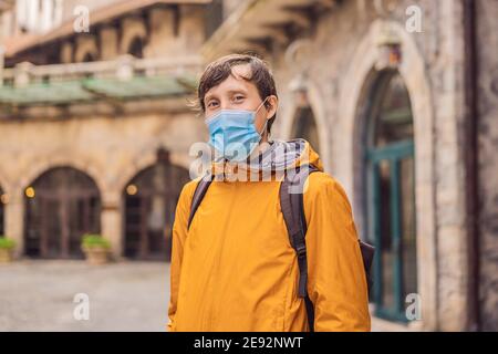 Giovane uomo che indossa una maschera medica durante il COVID-19 coronavirus turistico Passeggiate lungo la strada in una città europea dopo il Fine del coronavirus COVID-19 Foto Stock