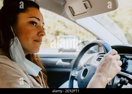 Donna seduta in auto elettrica mentre si guarda via durante COVID-19 Foto Stock