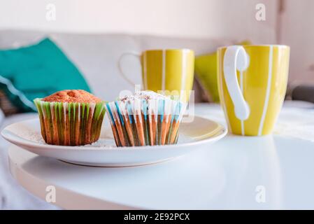 Cupcake con involucri colorati in primo piano, con tazze dietro. Snack nel soggiorno Foto Stock