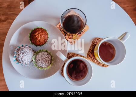 Cupcake e tazze con caffè fumante e tè su un piccolo tavolo bianco. Foto Stock