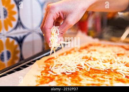 Spruzzare il formaggio grattugiato sul pomodoro a base di pizza. Foto Stock