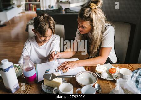 Madre che insegna il figlio mentre si ha la colazione in soggiorno Foto Stock