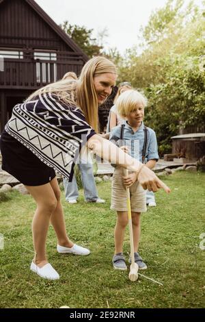 Madre che indica mentre si sta in piedi da un figlio che gioca polo di fronte iarda Foto Stock