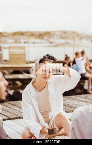 Giovane donna che protegge gli occhi mentre si siede con gli amici durante il picnic il giorno di sole Foto Stock