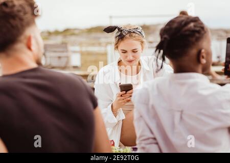 Donna sorridente che usa lo smartphone con gli amici durante il picnic Foto Stock