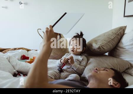 Libro di lettura del padre con il figlio del bambino che si trova sul letto a. casa Foto Stock