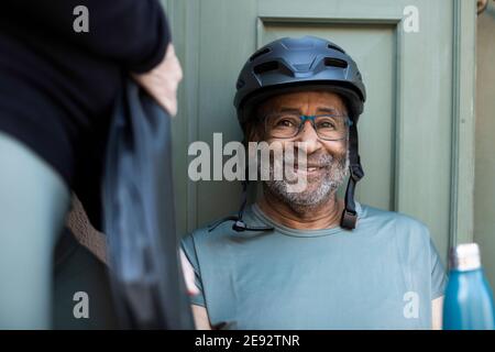 Uomo anziano sorridente con bottiglia contro la porta Foto Stock