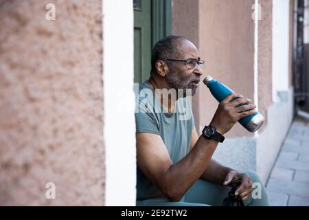 Uomo anziano che beve acqua dalla bottiglia fuori casa Foto Stock
