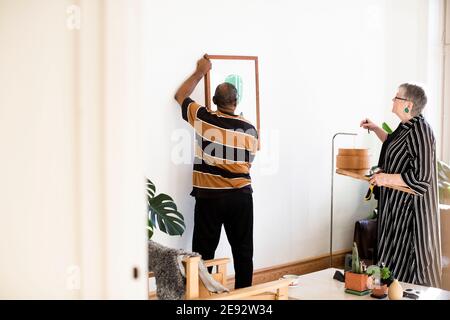 Uomo anziano che regola la pittura mentre si sta contro la donna in vita camera Foto Stock