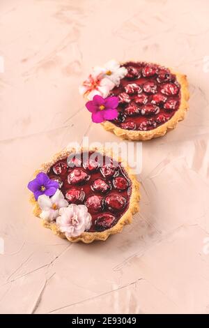 Mini torte primaverili fatte in casa con frutti di bosco decorati con fiori Foto Stock