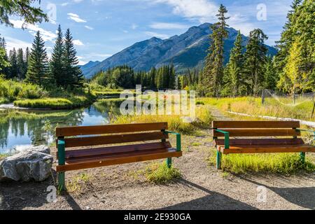 Panca in legno sul fiume Bow River. Percorso sul fiume Bow in estate. Monte Norquay sullo sfondo. Banff National Park, Canadian Rockies, Alberta, Foto Stock