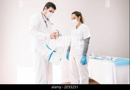 Medici di sesso maschile e femminile che indossano maschere in piedi insieme in medicina camera con costume protettivo da COVID 19 Foto Stock