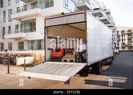 Carrello vuoto e non identificato con portellone aperto davanti agli edifici moderni. Carrelli elevatori e pacchi su pallet all'interno della spac di stoccaggio Foto Stock