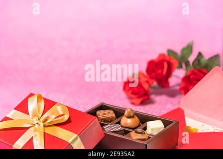 Biglietto d'auguri per San Valentino o giorno bianco raffigurante una scatola di cioccolato adornato con un nastro dorato e una lettera d'amore con fiori di rose rosse su una p scintillante Foto Stock