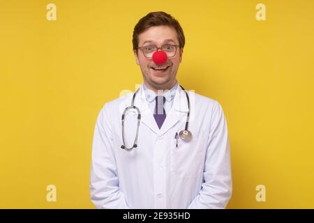 Divertente medico caucasico con il naso rosso pagliaccio sorridente alla macchina fotografica. Scatto in studio Foto Stock