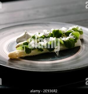 Piatto di asparagi bianchi cotti placcati e decorati con bianco fiori e crema sul lato di un ristorante Foto Stock