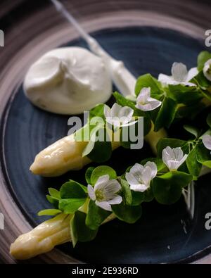 Piatto di asparagi bianchi cotti placcati e decorati con bianco fiori e crema sul lato di un ristorante Foto Stock