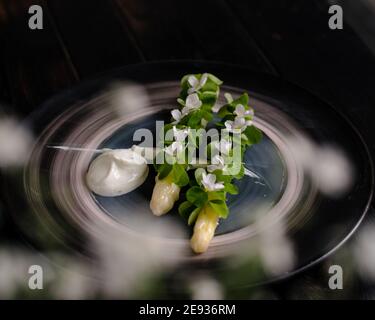 Piatto di asparagi bianchi cotti placcati e decorati con bianco fiori e crema sul lato di un ristorante Foto Stock