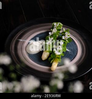 Piatto di asparagi bianchi cotti placcati e decorati con bianco fiori e crema sul lato di un ristorante Foto Stock