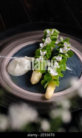 Piatto di asparagi bianchi cotti placcati e decorati con bianco fiori e crema sul lato di un ristorante Foto Stock