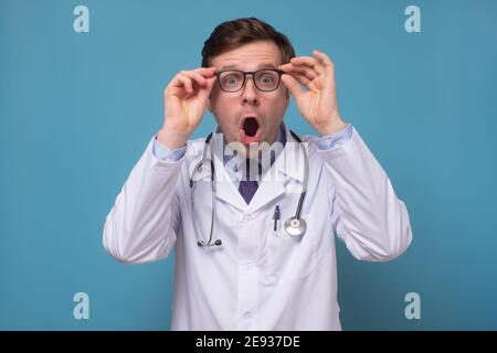 Uomo ispanico adulto che indossa uniforme medico e stetoscopio con sorpresa e stupito espressione sul viso. Scatto in studio Foto Stock