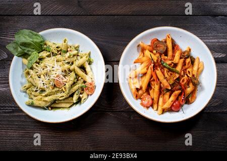 Rigatoni arrabiata e Rigatoni Pesto su un tavolo di legno marrone con una forcella e un coltello Foto Stock
