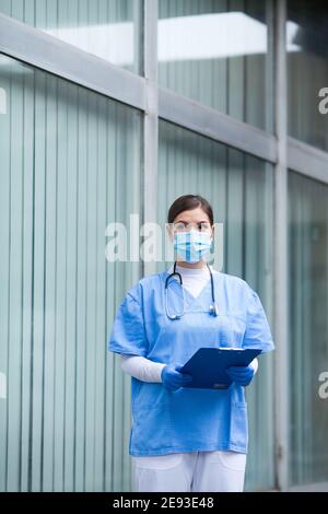 Donna paramedica EMS UK che indossa dispositivi di protezione individuale DPI Holding Appunti, di fronte al sito di test PCR dell'ospedale di terapia intensiva, COVID-19 pandemi Foto Stock