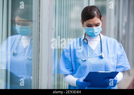 Donna ICU medico controllo paziente cartella clinica clipboard scheda, prima Soccorritore chiave operatore medico, servizio di triage di emergenza durante la COV Foto Stock