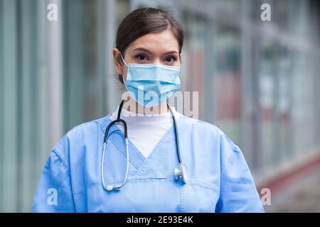 Giovane preoccupato sollecitato ansioso donna EMS lavoratore chiave medico, infelice ritratto Di fronte alla struttura sanitaria NHS del Regno Unito UTI, GP indossare protettivo Faccia PPE Foto Stock