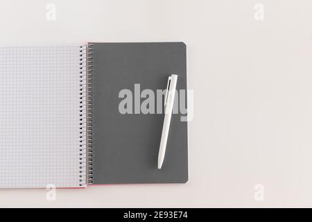 Notebook con apertura a spirale con foglio grigio e penna bianca. Layout e disposizione piatta con posizione per il testo isolato su sfondo bianco. Ritorno a scuola. Vista dall'alto, Foto Stock