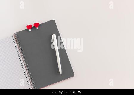 Taccuino a spirale aperto con foglio grigio con due spicchi a forma di cuore e penna bianca su sfondo bianco. Mock up per San Valentino, amore e r Foto Stock