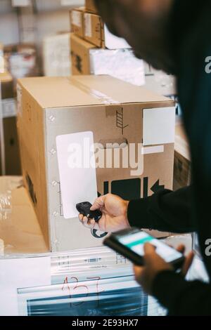 Immagine ritagliata di un lavoratore maschio che scansiona una scatola di cartone con barra lettore di codici presso il magazzino di distribuzione Foto Stock