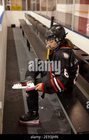 Ragazza giocatore di hockey mettere guardie su pattini di ghiaccio Foto Stock