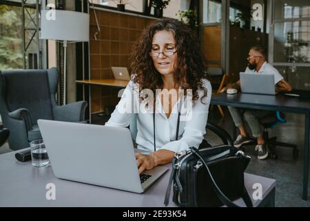 Donna d'affari matura che lavora su un computer portatile mentre si siede in una nuova azienda Foto Stock