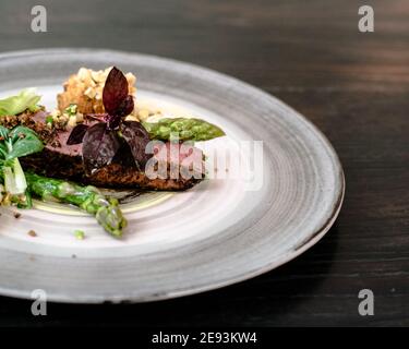 Piatto di bistecca di struzzo con asparagi bianchi e verdi, verdure da giardino e salsa su un piatto su un tavolo di legno in un ristorante Foto Stock