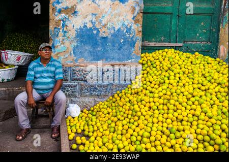 Un mercante colombiano si trova accanto a un mucchio di arance verdi (per la spremitura) in un mercato della frutta all'aperto a Barranquilla, Colombia. Foto Stock