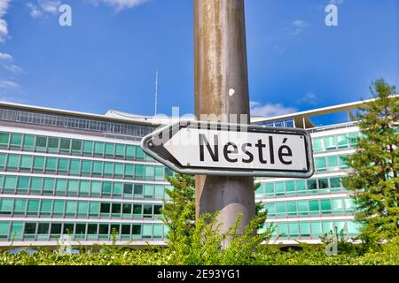 Vevey, Svizzera - 14 agosto 2020: Cartello che indica Nestlé in primo piano e Nestlé HQ edificio sullo sfondo. Nestle è la più grande multinazionale Foto Stock