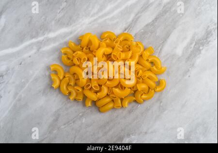 Pila di macaroni a gomito organici su un piano di marmo grigio illuminato con luce naturale. Foto Stock