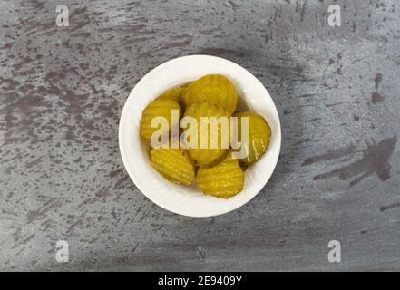 Vista dall'alto di una piccola ciotola bianca piena di fette di aneto di hamburger su un tavolo grigio illuminato con luce naturale. Foto Stock