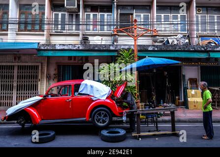 Un uomo guarda mentre un meccanico di automobile maschile lavora su un vecchio betle di VW in una strada nella zona di Chinatown di Bangkok, Thailandia Foto Stock