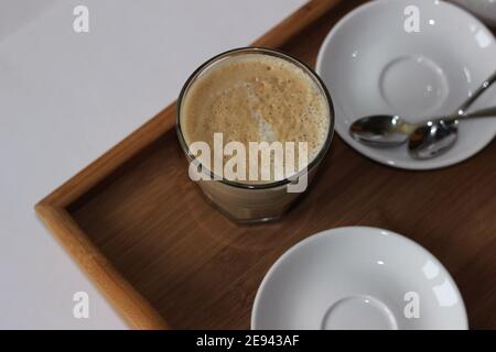 Bicchiere di bianco piatto servito su vassoio di legno. Caffè del mattino. Foto Stock