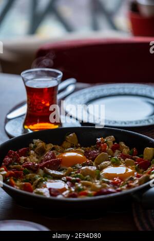 Uova strapazzate con cipolle tritate, pomodori e peperoni verdi a fette con un bicchiere di tè Foto Stock