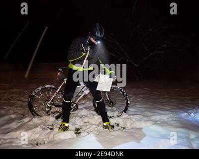 MTB rider controllare la mappa e chiamare un amico. Ciclista estrema equitazione mountain bike in volo neve durante la sera o la notte d'inverno. Foto Stock