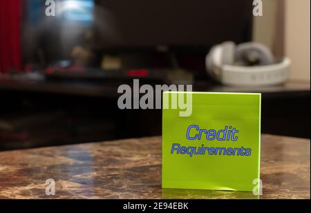Requisiti di credito. Testo su adesivo verde posizionato su un tavolo in marmo contro uno sfondo offuscato dell'ufficio domestico. Foto Stock