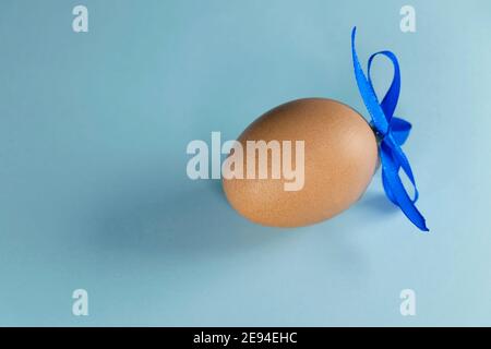 Uova di colore marrone con nastro blu. Buon concetto di Pasqua. Un uovo con nastro su sfondo blu pastello con spazio per la copia. Foto Stock